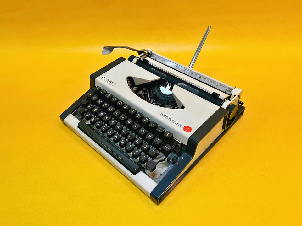 Front-side view of a 1970s Olympia Traveller Deluxe manual typewriter in Arctic White with a dark grey keyboard mask against a yellow background.