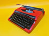 Front-side view of a vibrant Racing Red Silver Reed Silverette II manual typewriter with paper in the carriage against a yellow background.