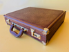 Front view of a luxury Tobacco Brown full-quill ostrich leather suitcase from the 1970s against a yellow background