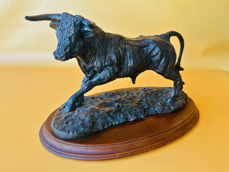 Vintage resin bull sculpture mounted on a wooden display base, featuring a dynamic charging pose and dark bronze-style finish.