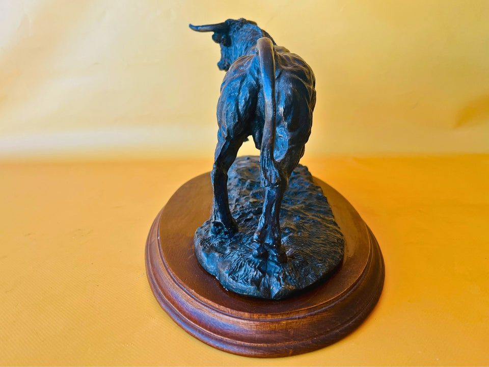 Side profile of a decorative resin bull figurine on a wooden plinth, showcasing the muscular body and realistic movement.