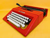 Front view of a vibrant Racing Red Olivetti College manual typewriter with high-contrast black keys against a yellow background.