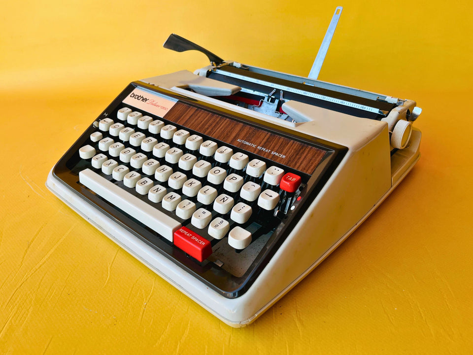 Front view of a crisp 1970s Brother Deluxe 1350 manual typewriter with its original hardshell case and printed instruction manual.