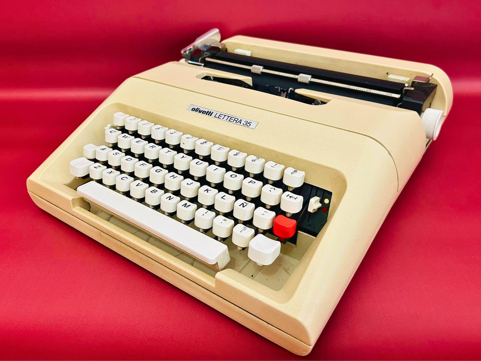 Front-side view of a classic sleek grey Olivetti Lettera 35 manual typewriter featuring a high-contrast white keyboard against a yellow background.