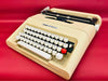 Front-side view of a classic sleek grey Olivetti Lettera 35 manual typewriter featuring a high-contrast white keyboard against a yellow background.