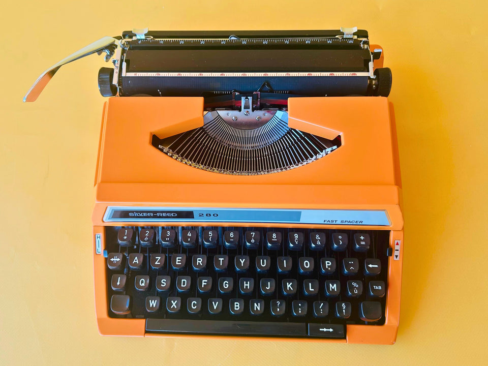 Detailed shot of the French AZERTY keyboard layout on an orange Silver Reed 280, featuring crisp black keys and the signature Fast Spacer bar.
