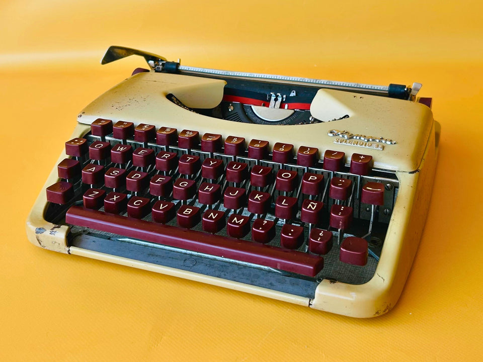 Front view of a vintage Olympia Splendid 33 manual typewriter with rare maroon keys against a bright yellow background.