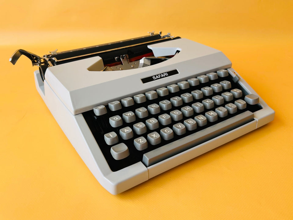 Front-side view of a 1960s Royal Safari manual typewriter in Slate Gray with a solid metal body and crisp black keyboard mask against a yellow background.