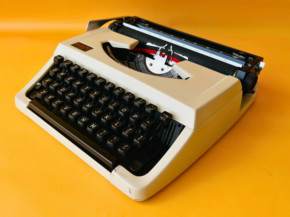 Angled view of an Arctic White Vendex 100 manual typewriter with its original black hard-shell carrying case.