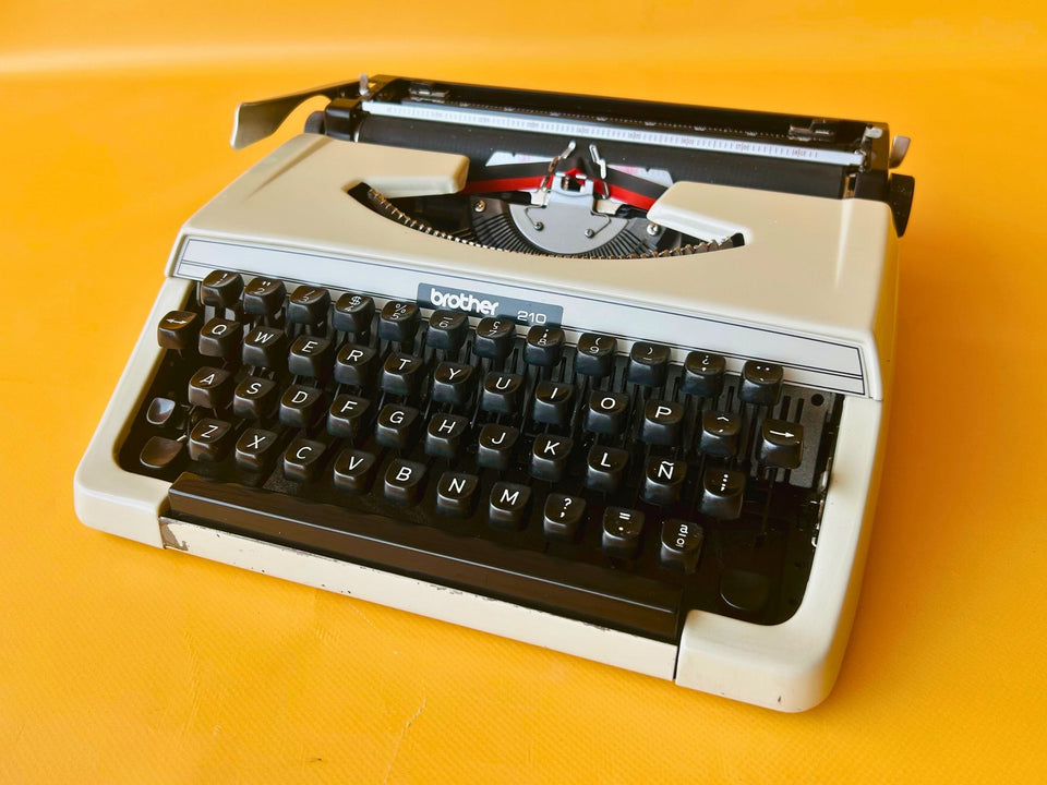 Front view of a crisp Arctic White Brother 210 manual typewriter with high-contrast black keys against a yellow background.