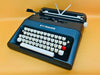 Front-side view of a sleek Matte Black Olivetti Lettera 35 manual typewriter with high-contrast white keys against a yellow background.