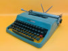 Front-side view of a classic Teal Blue Olivetti Lettera 32 manual typewriter against a vibrant yellow background.