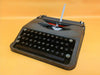 Front view of a 1960s Seafoam Green Hermes Baby manual typewriter in its iconic slim metal case against a yellow background.