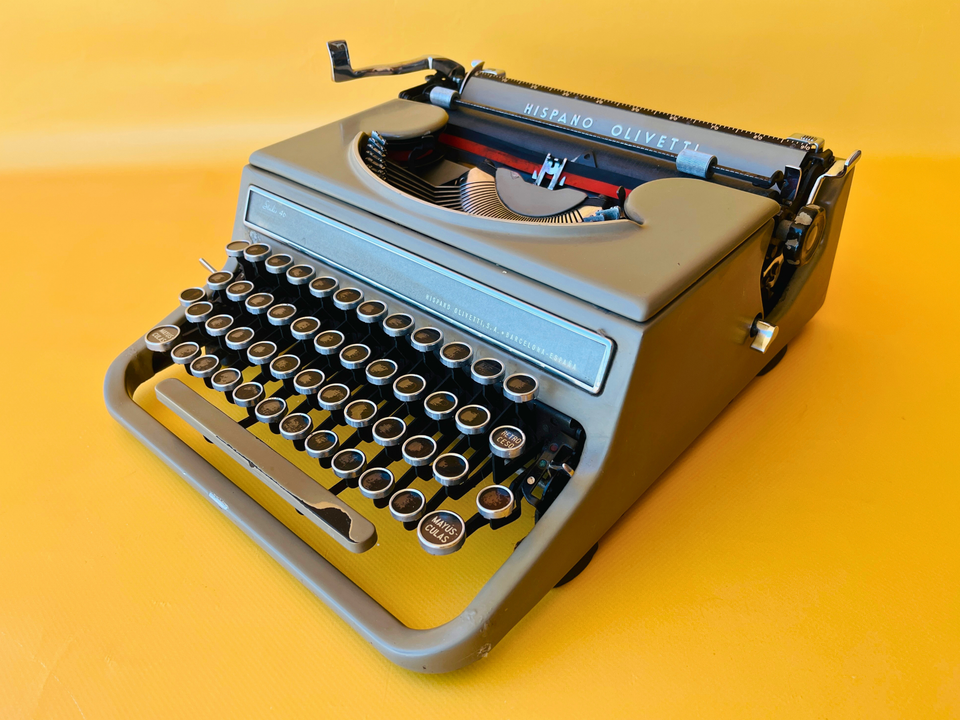 Front-side view of a 1940s Hispano Olivetti Studio 46 in sage green with naturally darkened vintage keys against a yellow background.