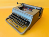 Front-side view of a 1940s Hispano Olivetti Studio 46 in sage green with naturally darkened vintage keys against a yellow background.