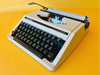 Front view of a crisp Arctic White Silver Reed SR 10 manual typewriter with its matching white hardshell case against a yellow background.