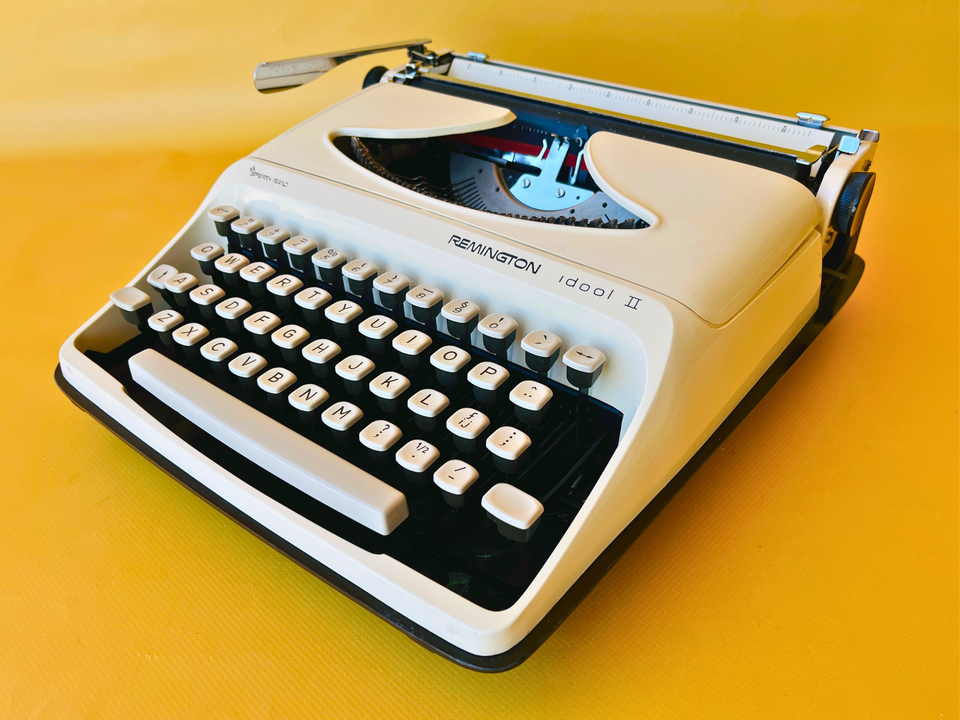 Front-side view of a 1970s Remington Idool 2 manual typewriter in a high-contrast white and dark grey finish against a yellow background.