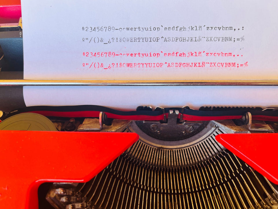 Close-up shot of a type sample sheet in the carriage rail, demonstrating perfect letter alignment and crisp, dark impressions in both black and red ink.