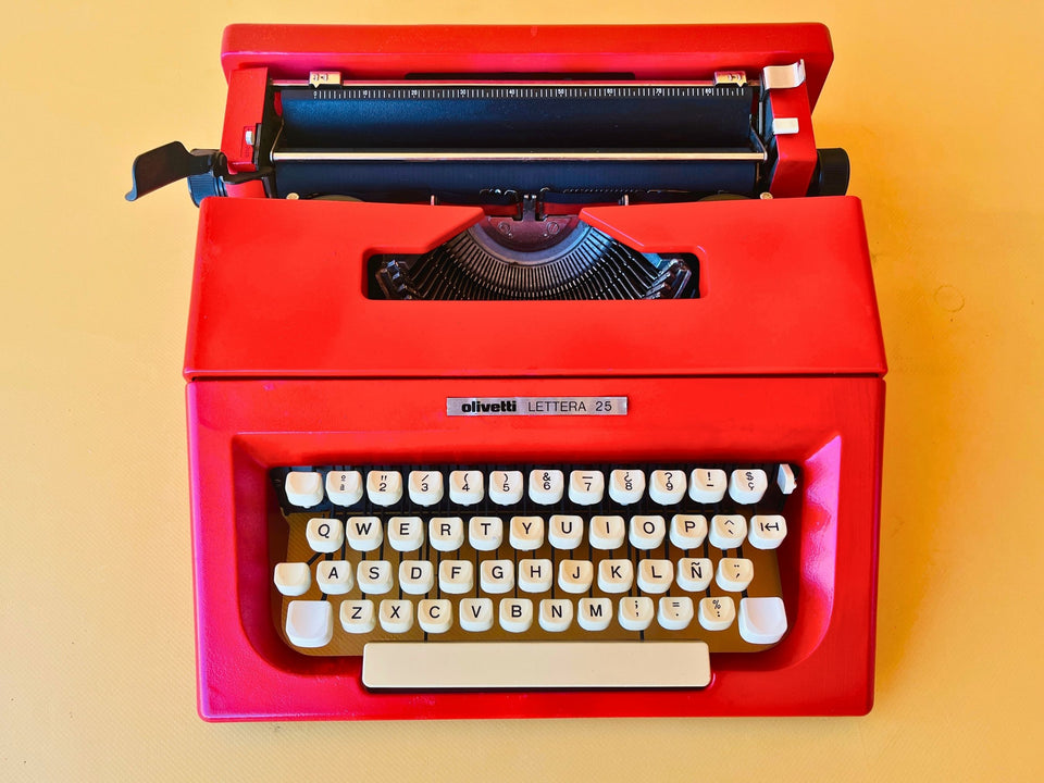 Top-down macro shot of the Spanish QWERTY keyboard on a red Olivetti Lettera 25, highlighting the flawless white keys, the 'Ñ' key, and the signature clean branding strip.