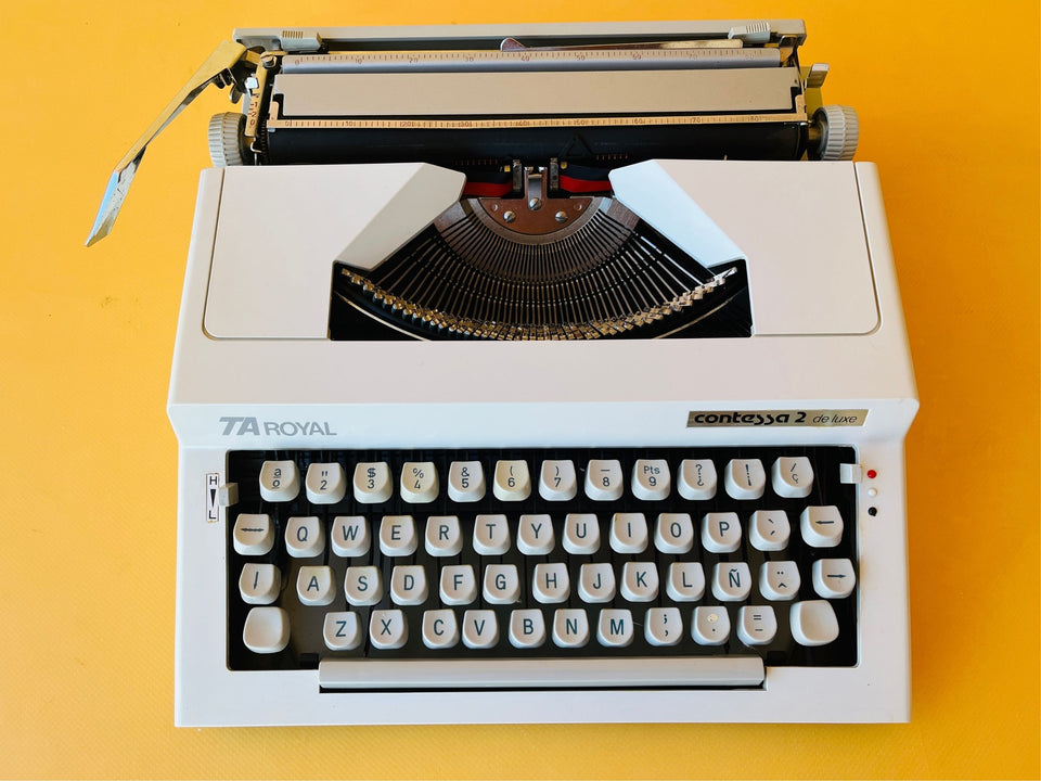 Detailed macro shot of the Spanish QWERTY keyboard on a Royal Contessa 2, showing the clean white block keys, the 'Ñ' key, and the distinct 'TA Royal' and 'Contessa 2 de luxe' branding badges.