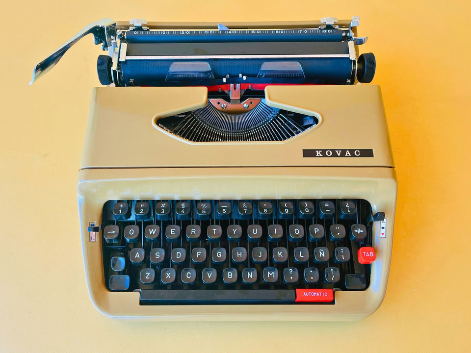 Close-up shot of the Spanish QWERTY keyboard on a gold-toned Kovac typewriter, highlighting the bright red 'AUTOMATIC' space accelerator key and the red 'TAB' key.