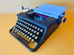 Front-three-quarter view of a vintage black Torpedo Modell 6 manual typewriter featuring glass-like keys against a yellow background