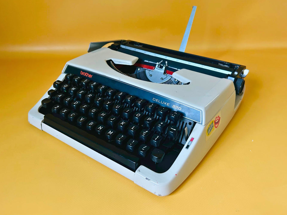 Vintage Brother Deluxe 220 portable typewriter in grey with English QWERTY keyboard displayed on yellow background