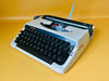 Vintage Brother Deluxe 220 portable typewriter in grey with English QWERTY keyboard displayed on yellow background