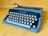 Blue Brother Deluxe portable typewriter with AZERTY keyboard displayed on yellow background