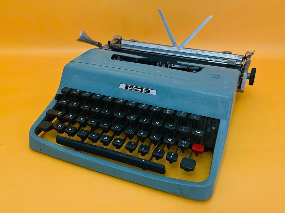 Blue Olivetti Lettera 32 portable typewriter with AZERTY keyboard displayed on yellow background