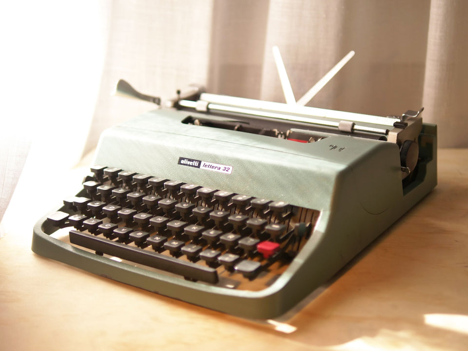 Front-side view of a classic blue-green Olivetti Lettera 32 manual typewriter in excellent condition with paper in the carriage
