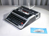 Front view of a mint condition black leather-clad Olivetti Lettera DL typewriter with silver aluminum trim.